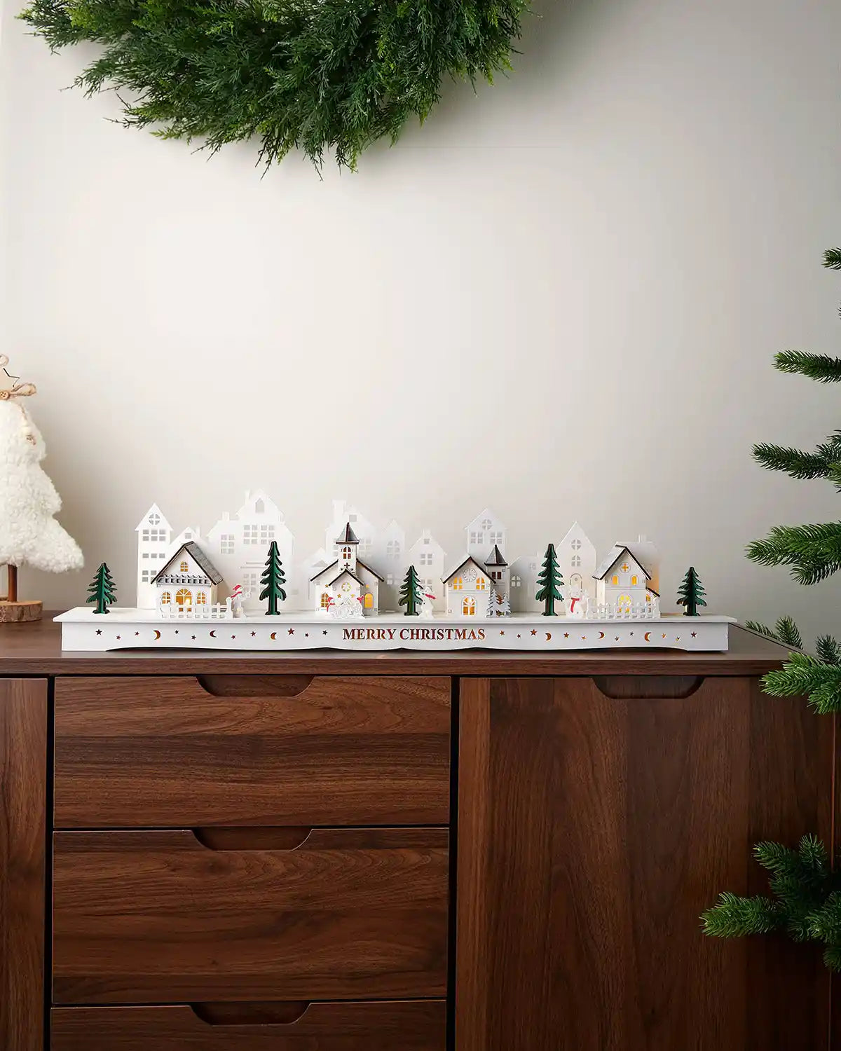 Alternative full image of pre-lit white wooden village with warm white light on dark wood surface in front of white wall