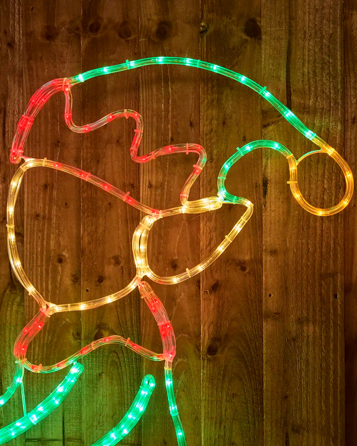 An Elf Christmas light outline shaped like Santa's hat, featuring warm white LED rope lights with green and red segments, displayed against a dark wood plank background.