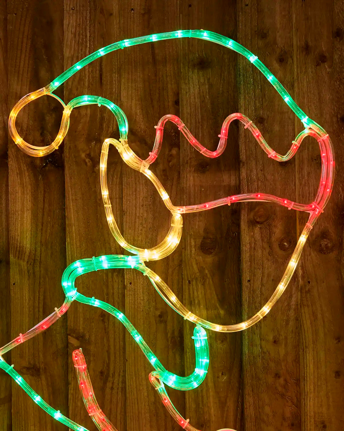 An Elf Christmas light outline shaped like Santa's hat, featuring warm white LED tubing with green and red segments, displayed against a dark wood plank background.