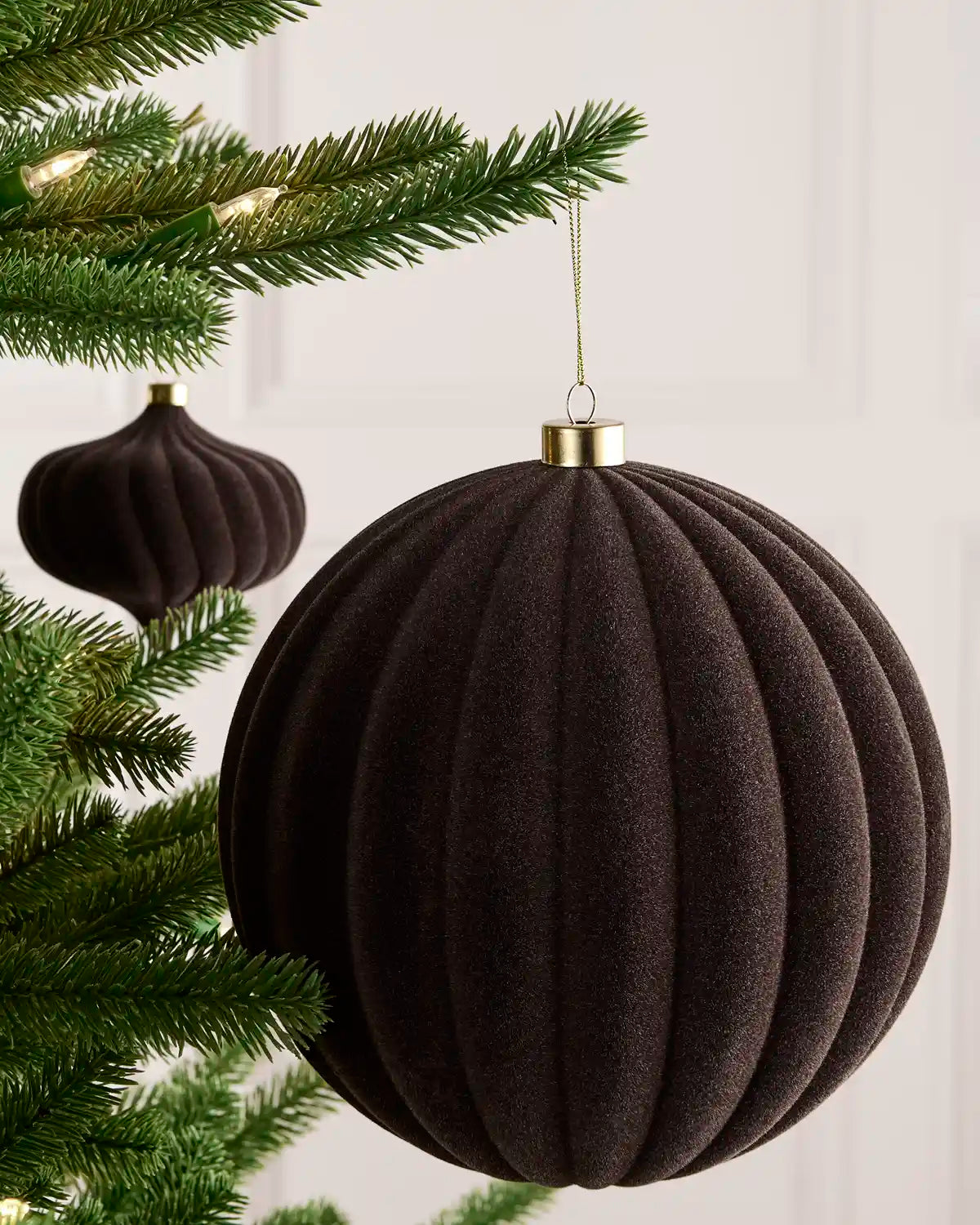 An espresso ribbed fabric Christmas ornament hanging from a green Christmas tree branch, with a smaller matching ornament in the background.