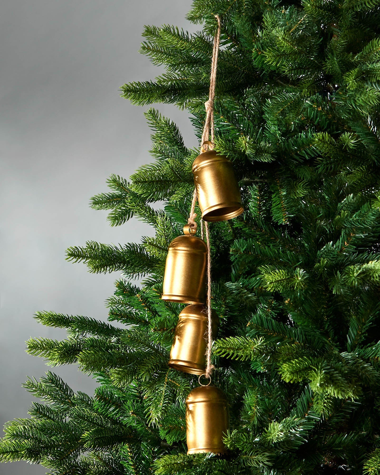 Antique-style gold hanging bells on Christmas tree in front of grey wall 