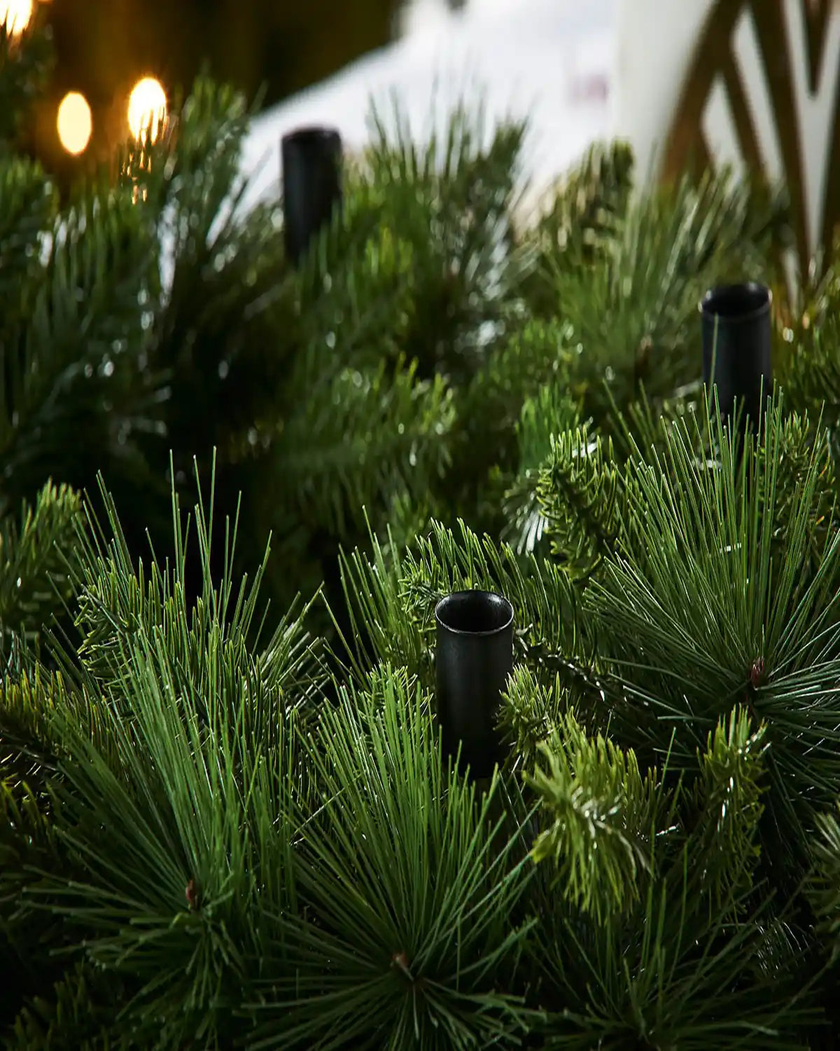 Artificial green wreath with black cylindrical candle holders in a blurred outdoor setting