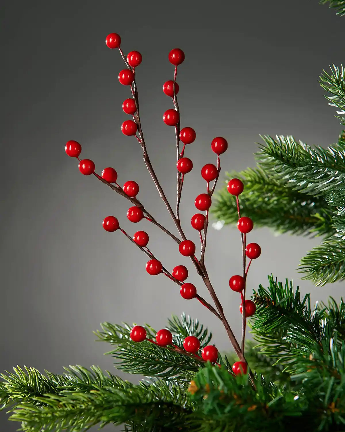 Artificial red berry branch with red berries on a grey background and a Christmas tree