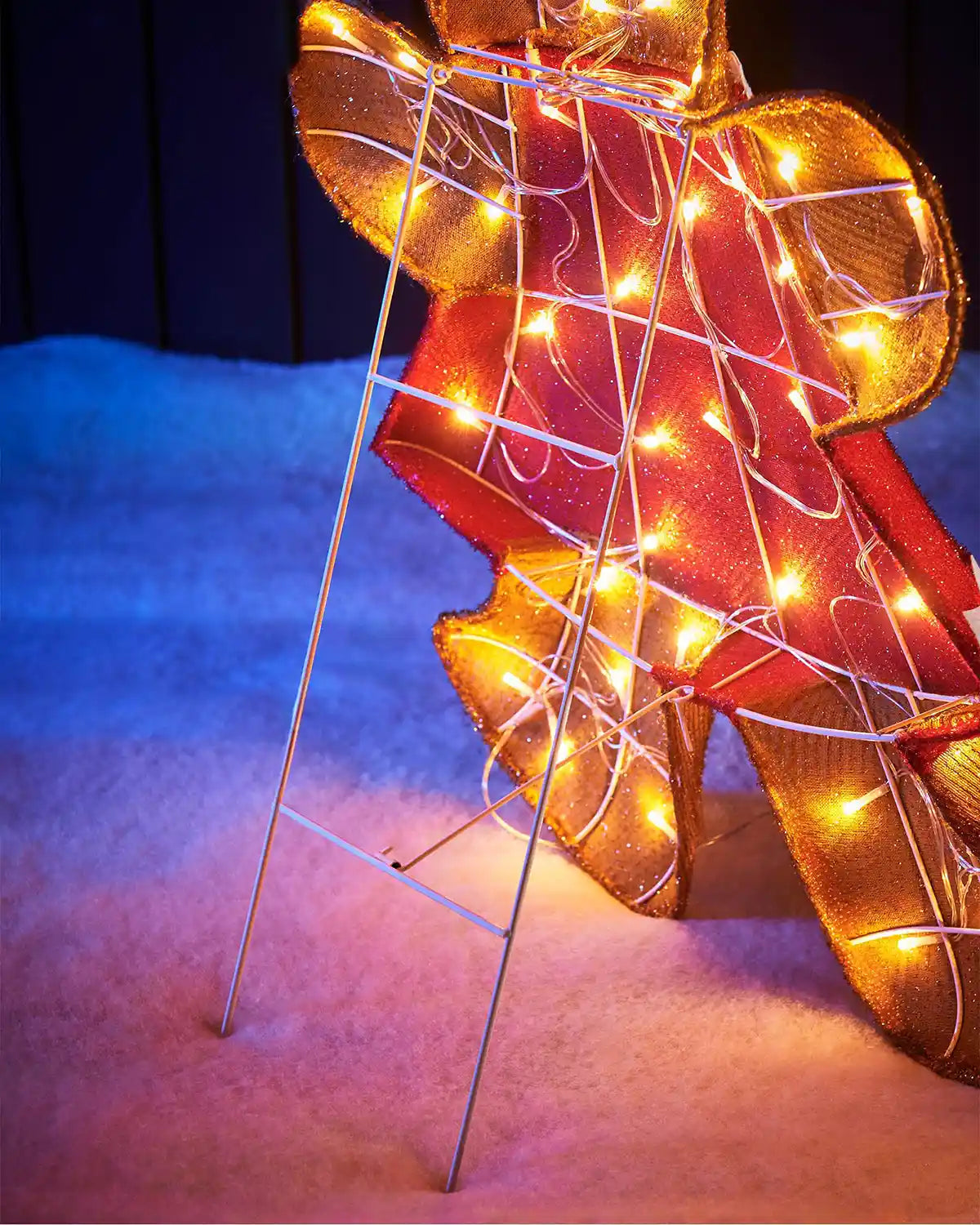 Back of LED gingerbread lady with red dress on snow grass and a dark background
