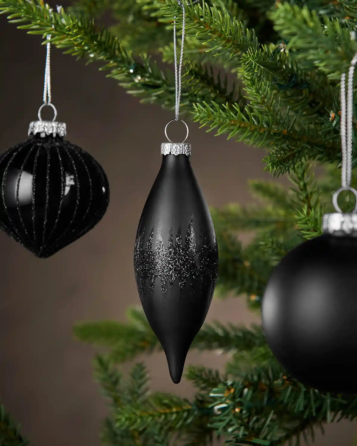 Black Christmas baubles hanging on a tree with a blurred background