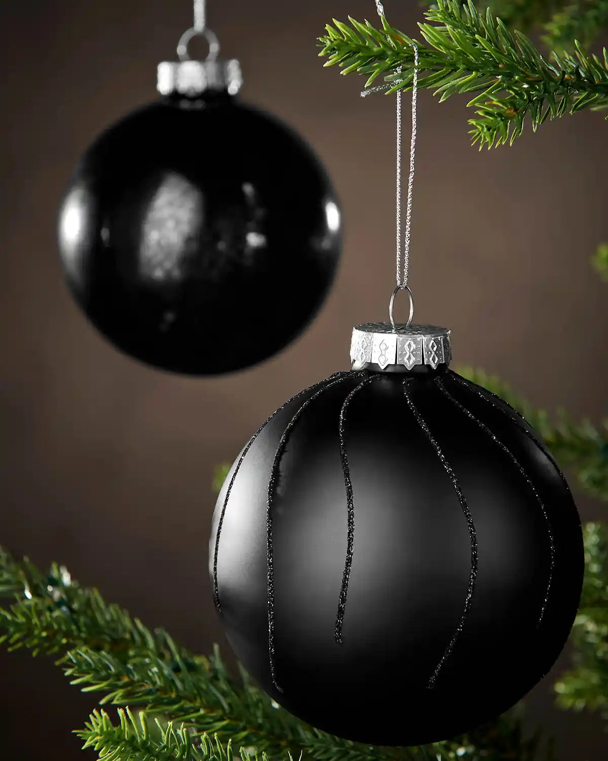 Black Christmas baubles hanging on a tree with a brown background
