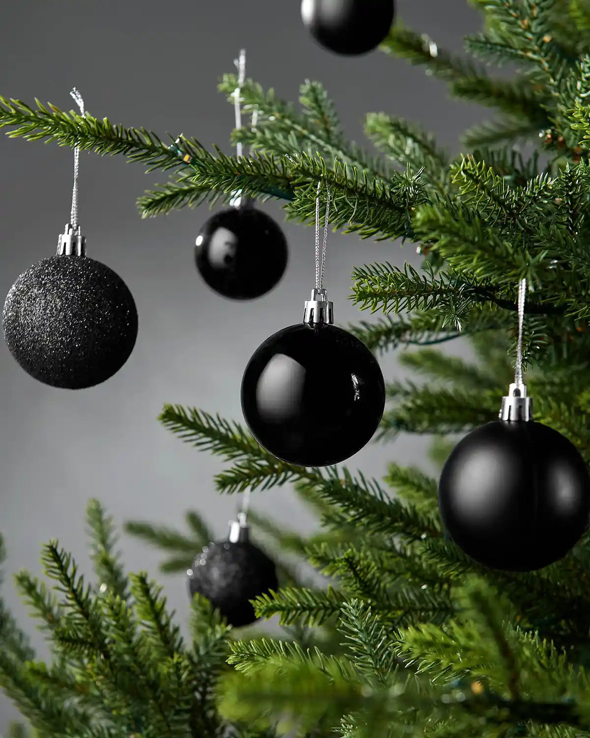 Black Christmas baubles on a green tree against a grey background