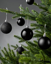 Black Christmas baubles on a green tree against a grey background