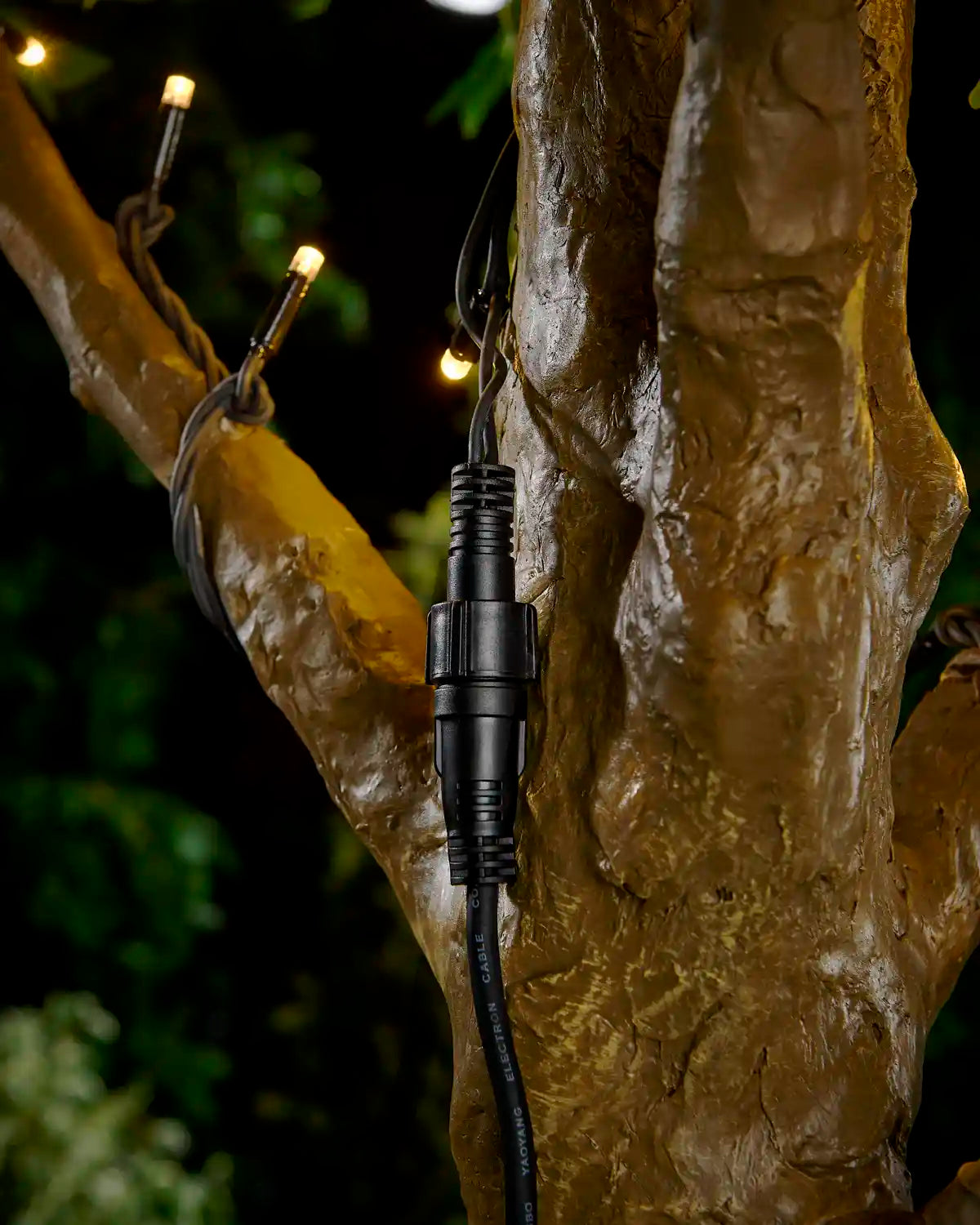 Black Pro Series connectable extension cable attached to a tree with warm white string lights