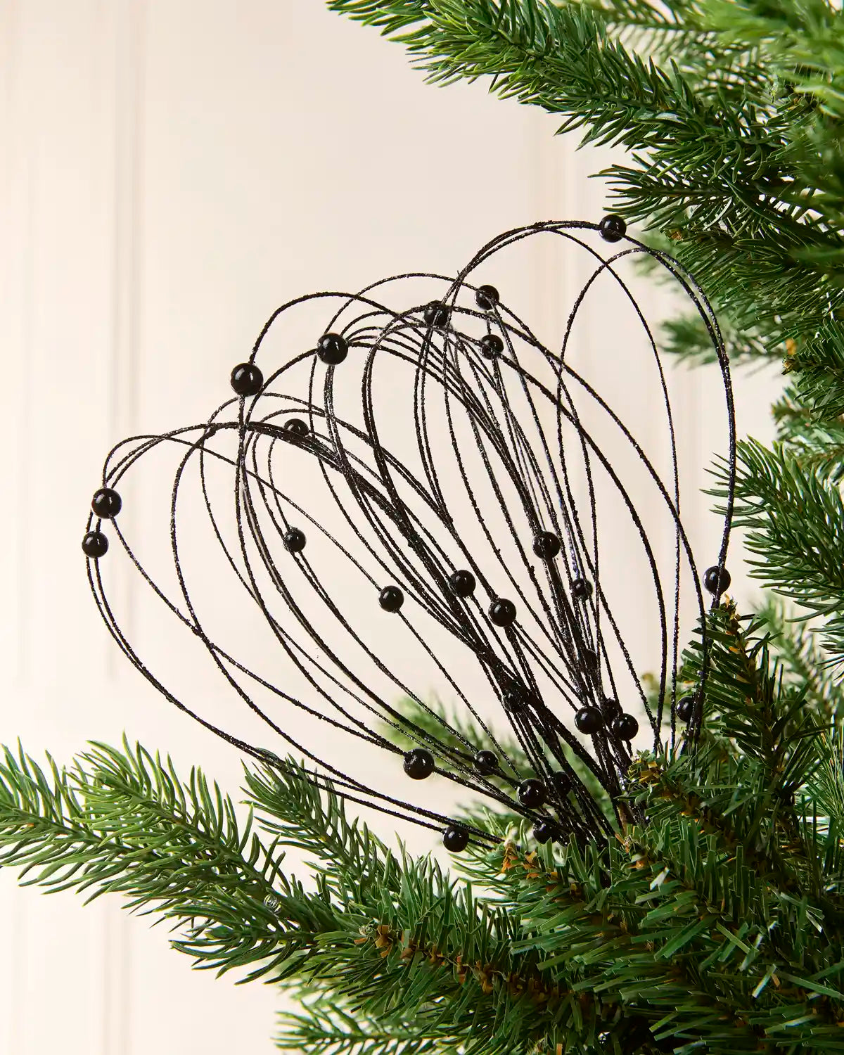 Black Glitter Nest Christmas Tree Pick placed in green Christmas tree branches with a cream background
