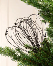 Black Glitter Nest Christmas Tree Pick placed in green Christmas tree branches with a cream background
