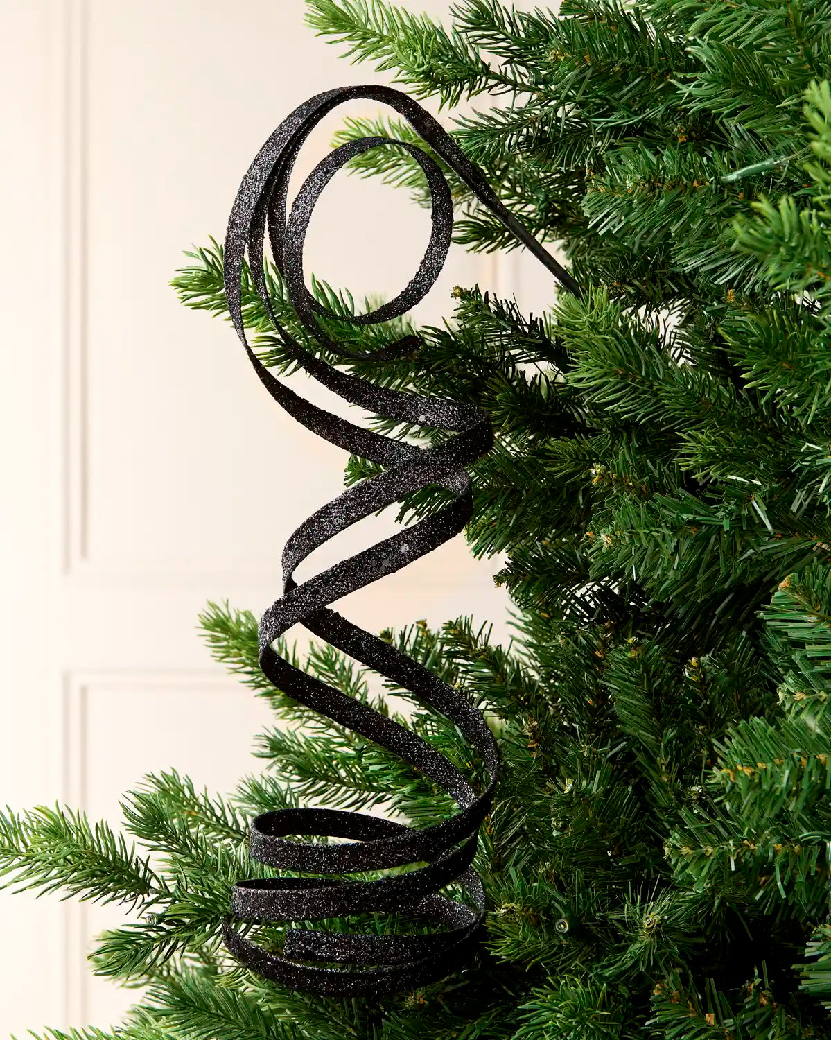 Black Glitter Spiral Swirl Pick hanging from Christmas tree branch with cream background
