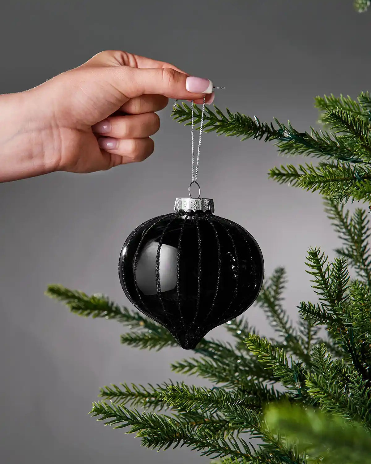 Black bauble being held on a branch against a grey background