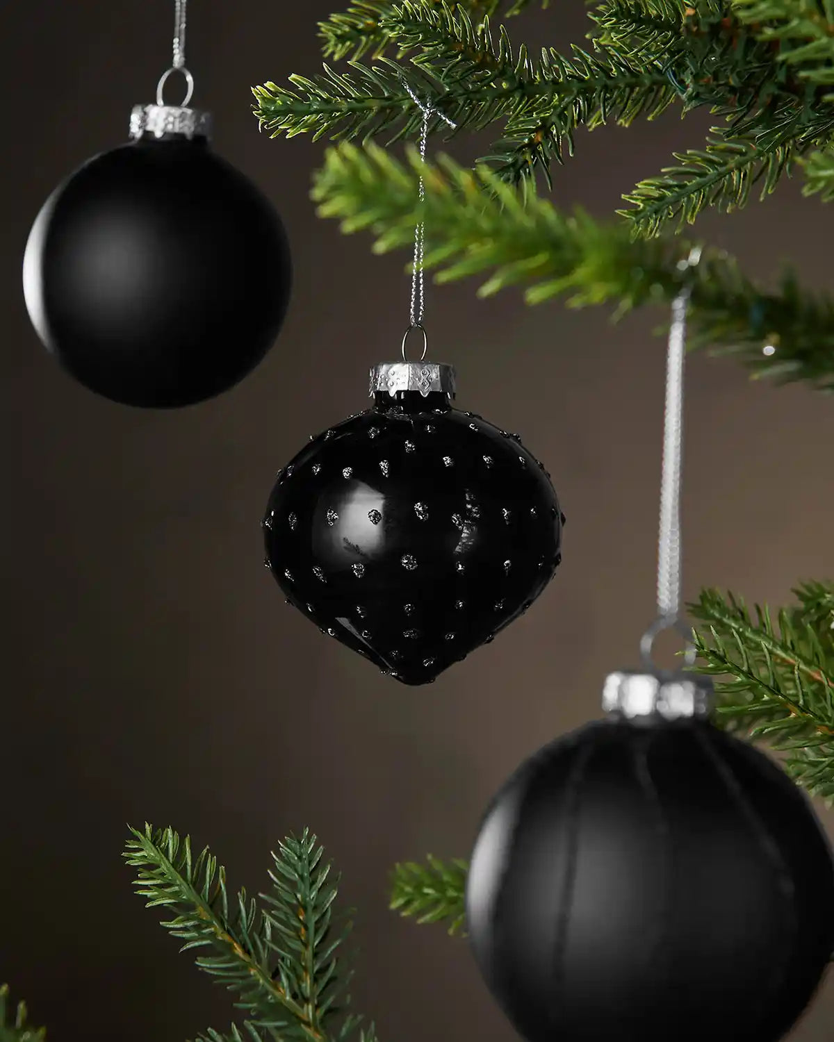 Black bauble with textured surface hanging on a Christmas tree branch.