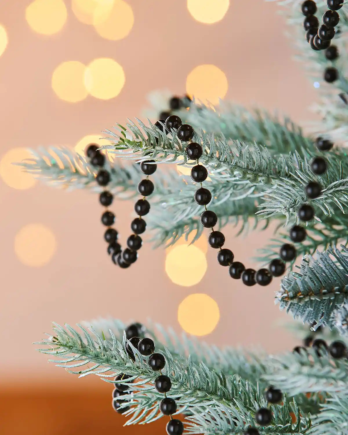 Black beaded garland on a Christmas tree branch with a blurred lights in the background