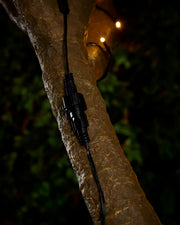 Black extension cable connection point with screw cap attached to tree with blurry LEDs in the background. 