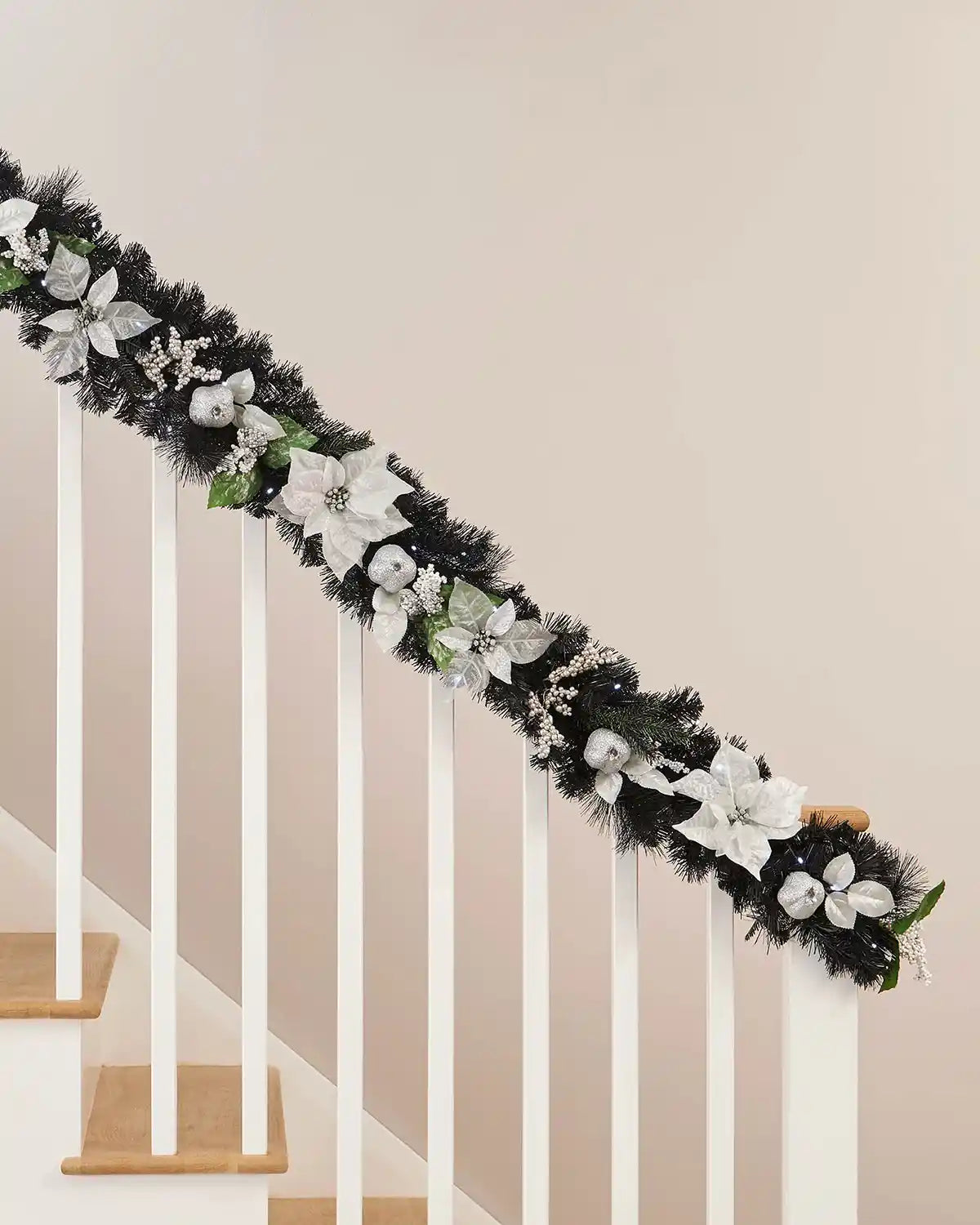 Black garland with interwoven bright white lighting and silver and white foliage resting upon a white wooden staircase