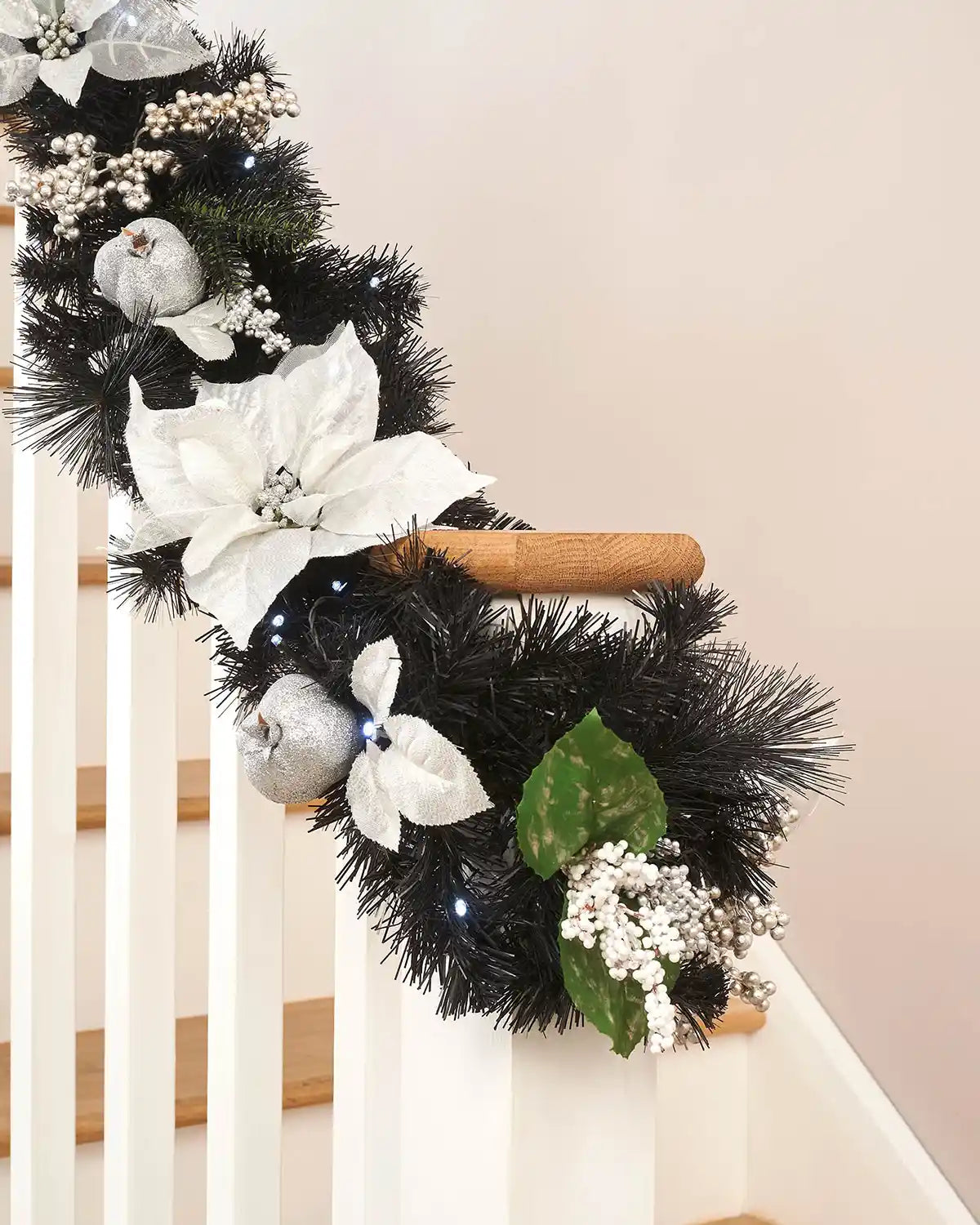 Close-up of black garland with interwoven bright white lighting and silver and white foliage wrapped around a wooden staircase