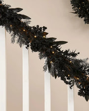 Black garland with warm white lights on a stair case banister against a cream wall