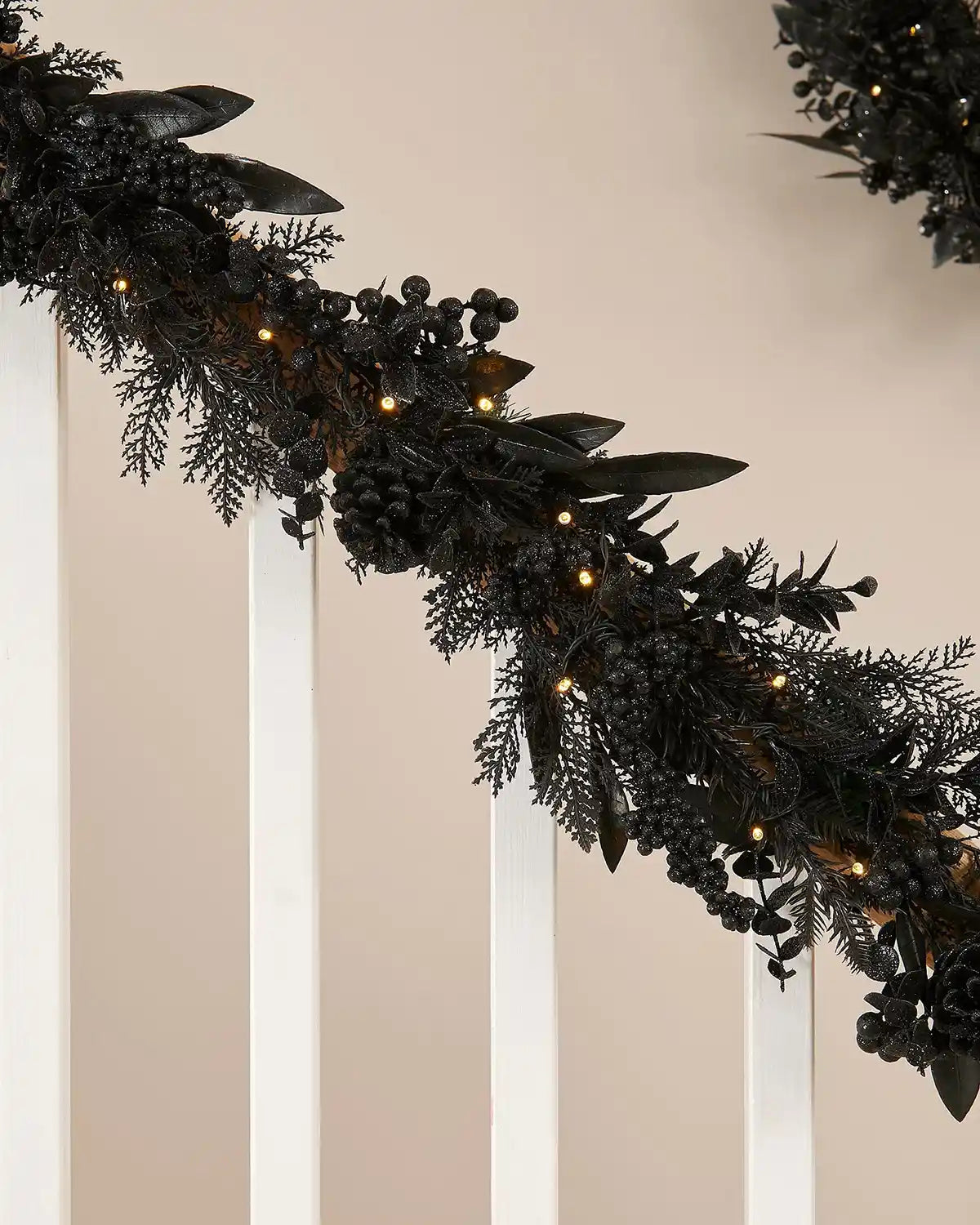 Black garland with warm white lights on a stair case banister against a cream wall