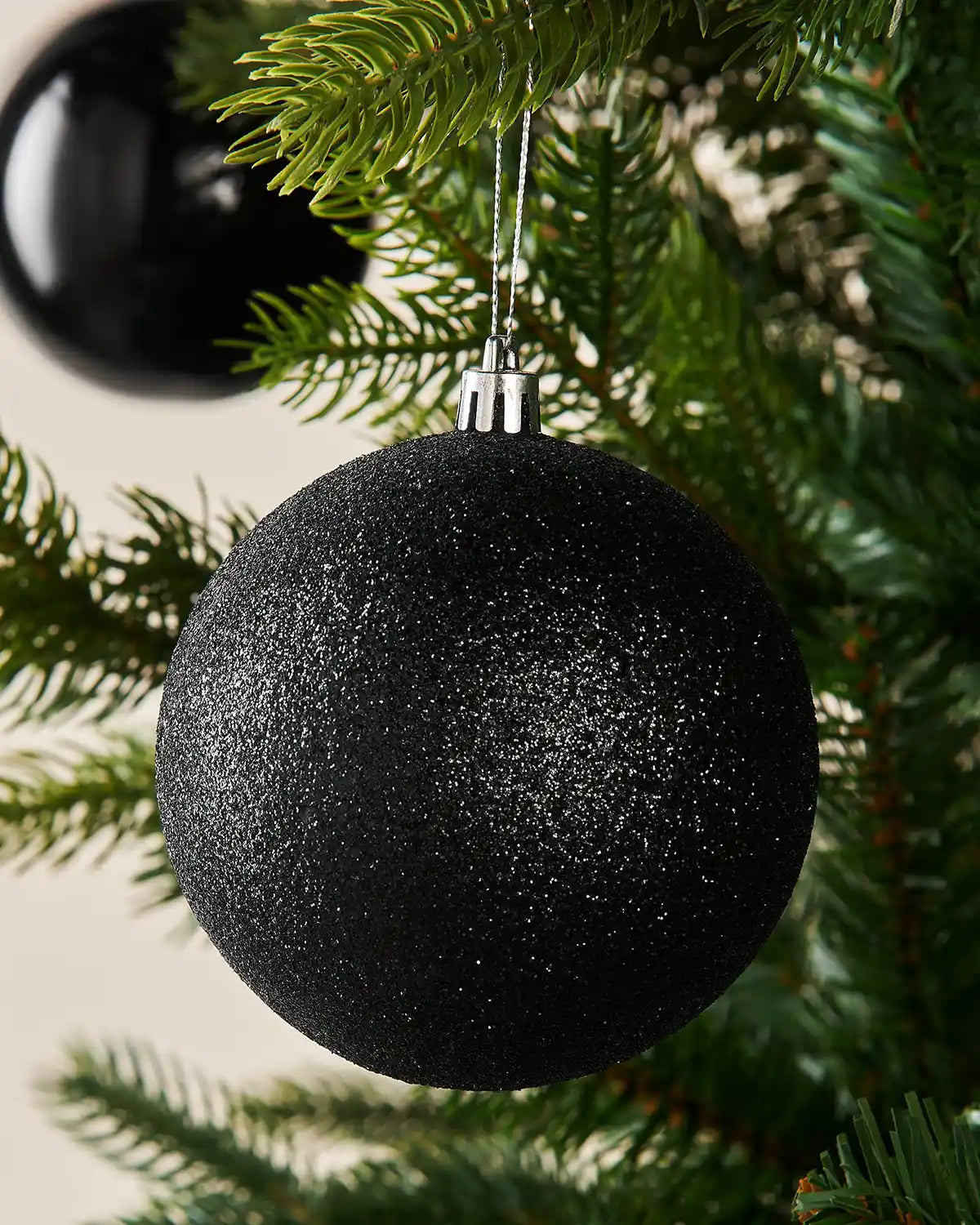 Black glittery Christmas ornament hanging on a tree branch