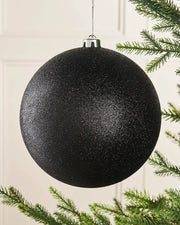 Black glittery oversized Christmas bauble on a Christmas tree branch 