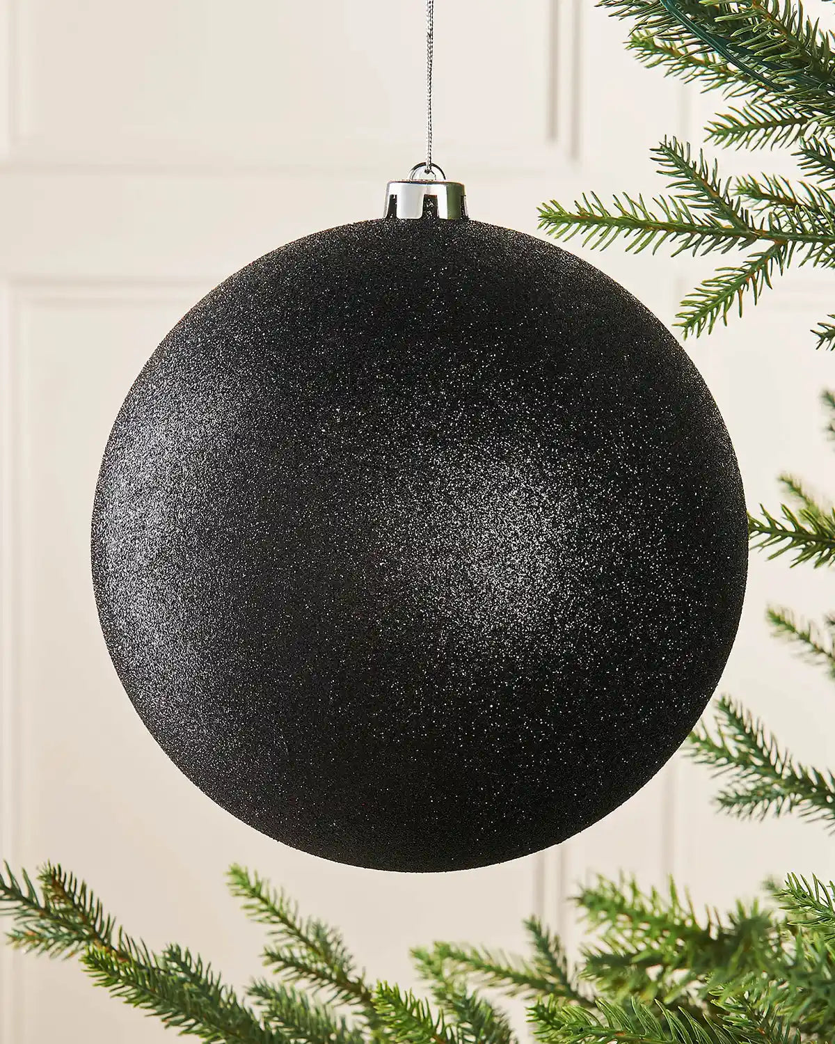 Black glittery oversized Christmas bauble on a Christmas tree branch 