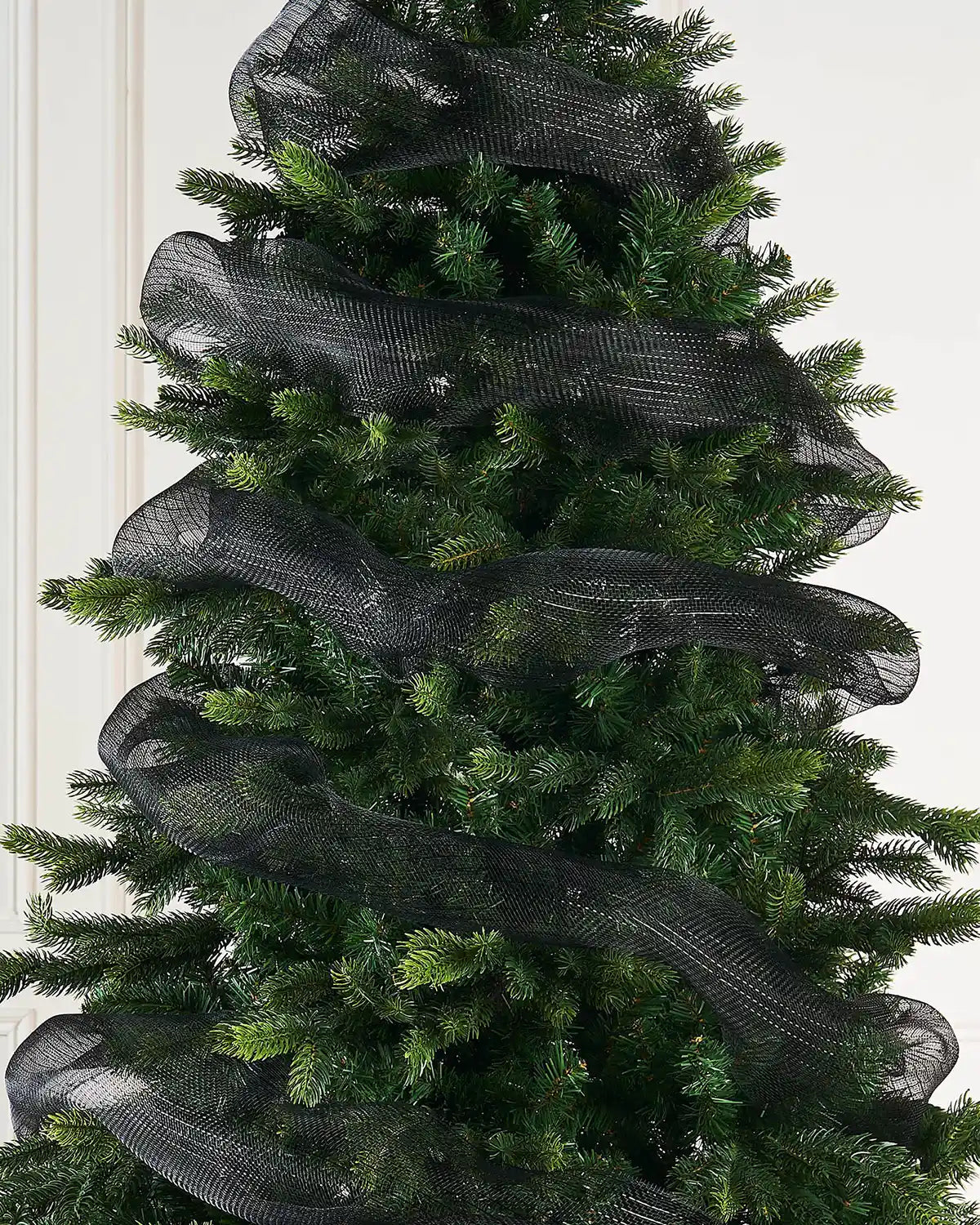 Black mesh ribbon wrapped around Christmas tree against a cream background