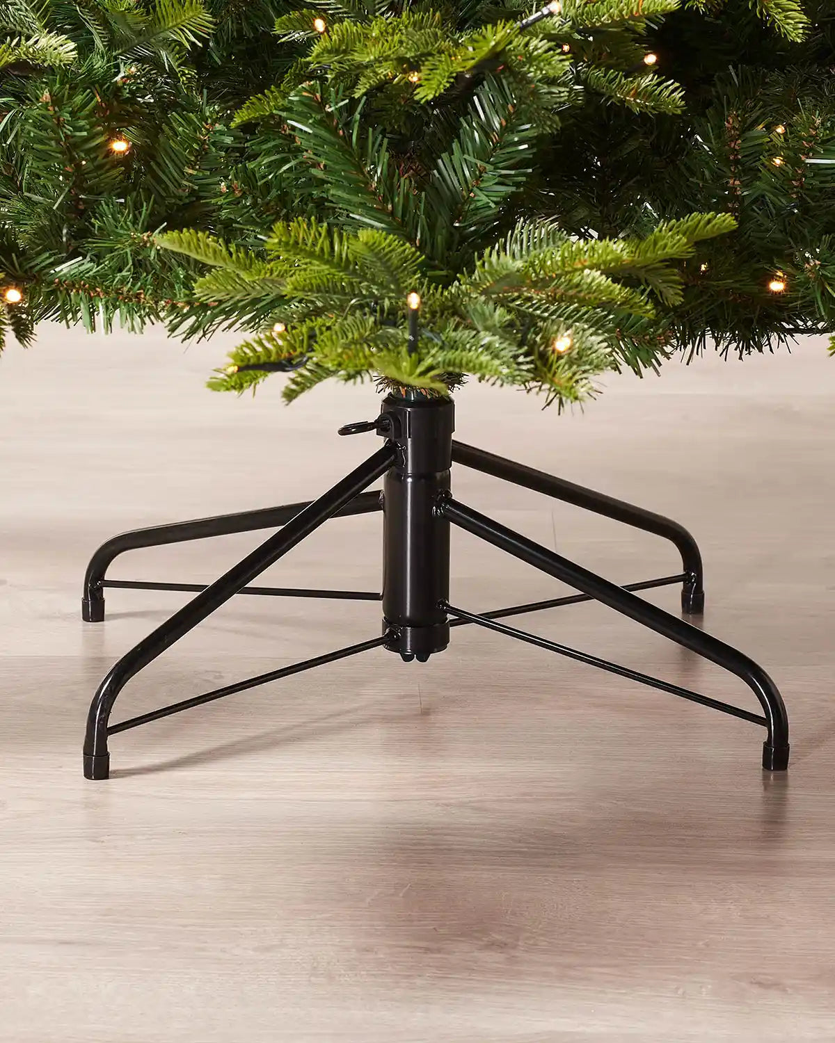 Black metal Christmas tree stand holding a Christmas tree on a wooden floor.
