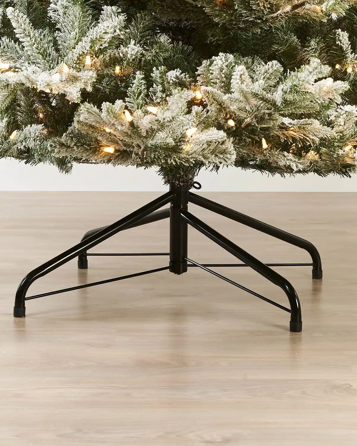 Black metal Christmas tree stand with a 9ft tree on a wooden floor.