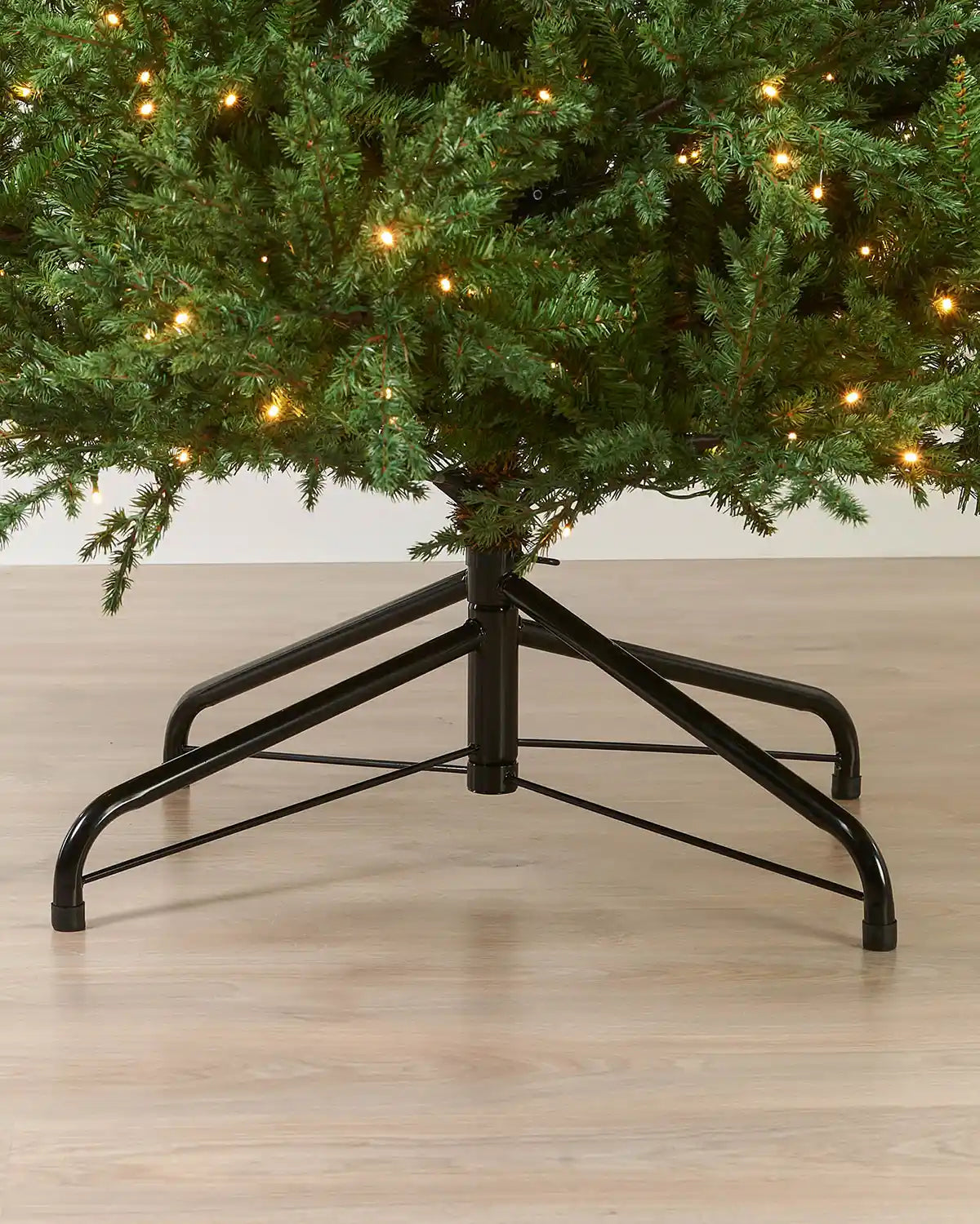 Black metal Christmas tree stand with a 9tf tree on a wooden floor.