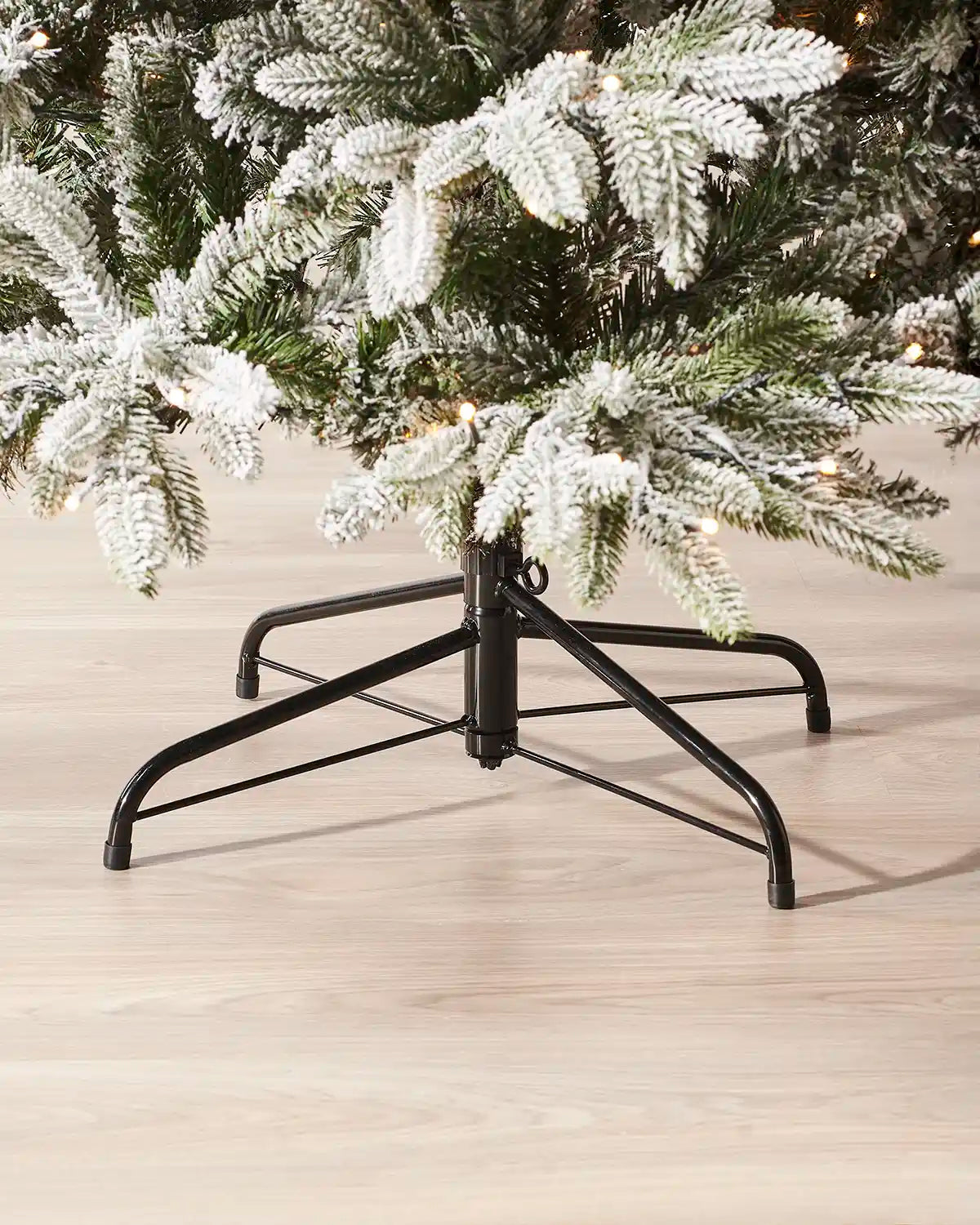 Black metal Christmas tree stand with a decorated tree on a wooden floor.