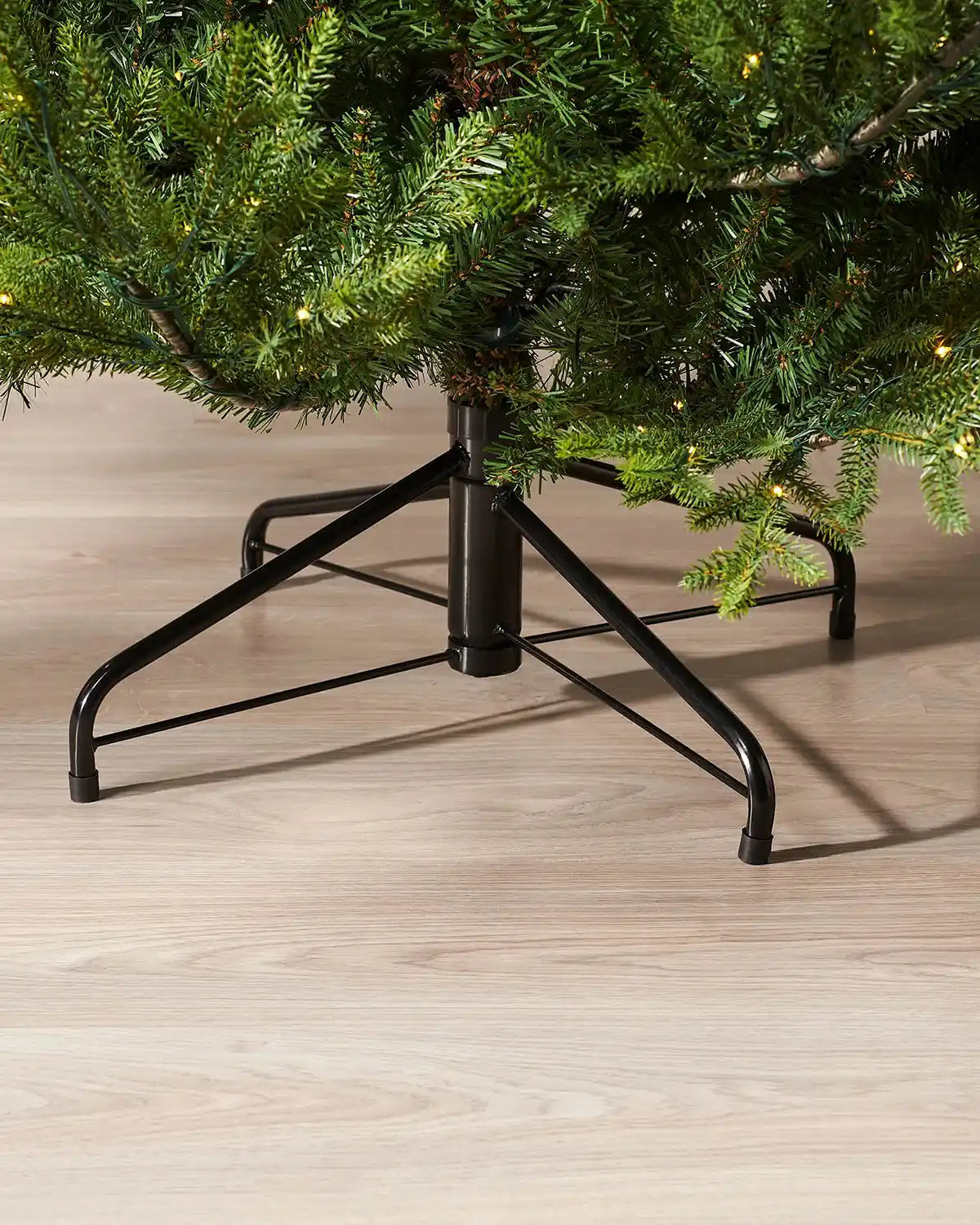Black metal tree stand holding a Christmas tree on a wooden floor.