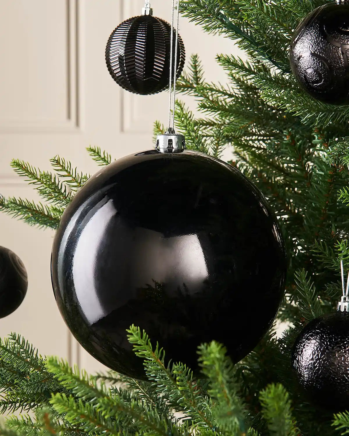 Black oversized gloss bauble on a Christmas tree branch with 4 smaller black baubles in the background