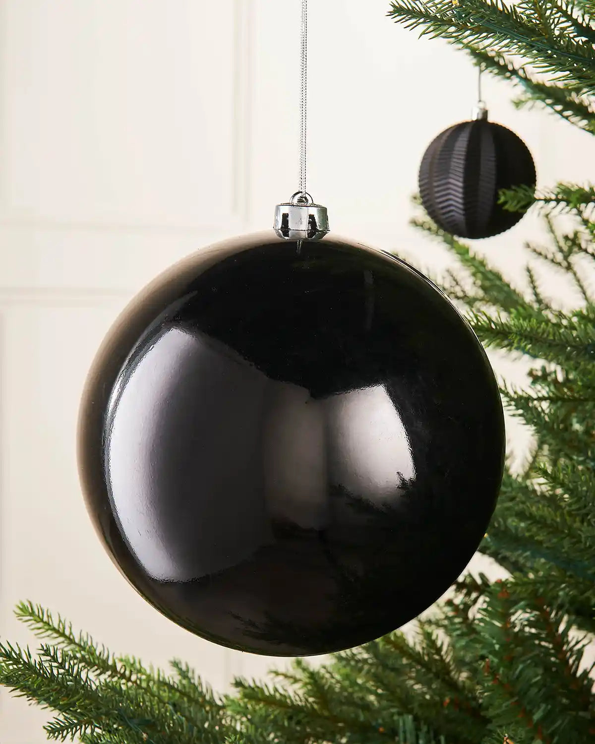 Black oversized gloss bauble on a Christmas tree branch with a smaller black bauble in the background