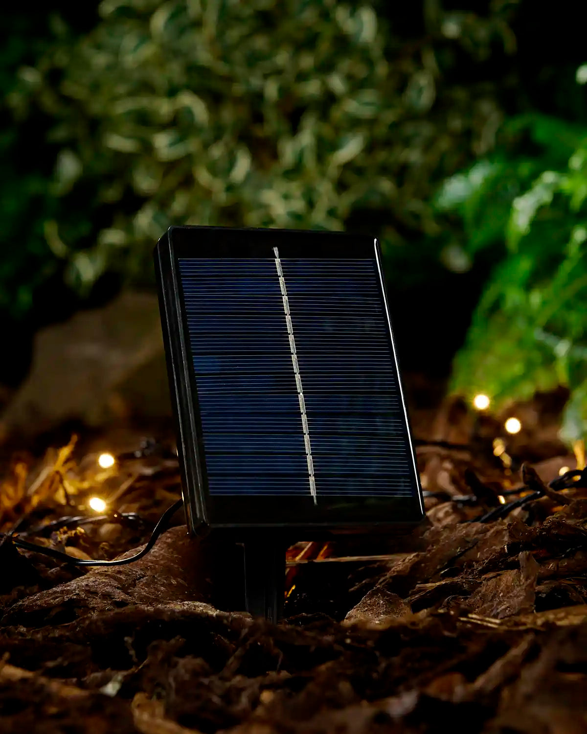 Black small solar panel in the ground with warm white LEDs and a blurred garden background