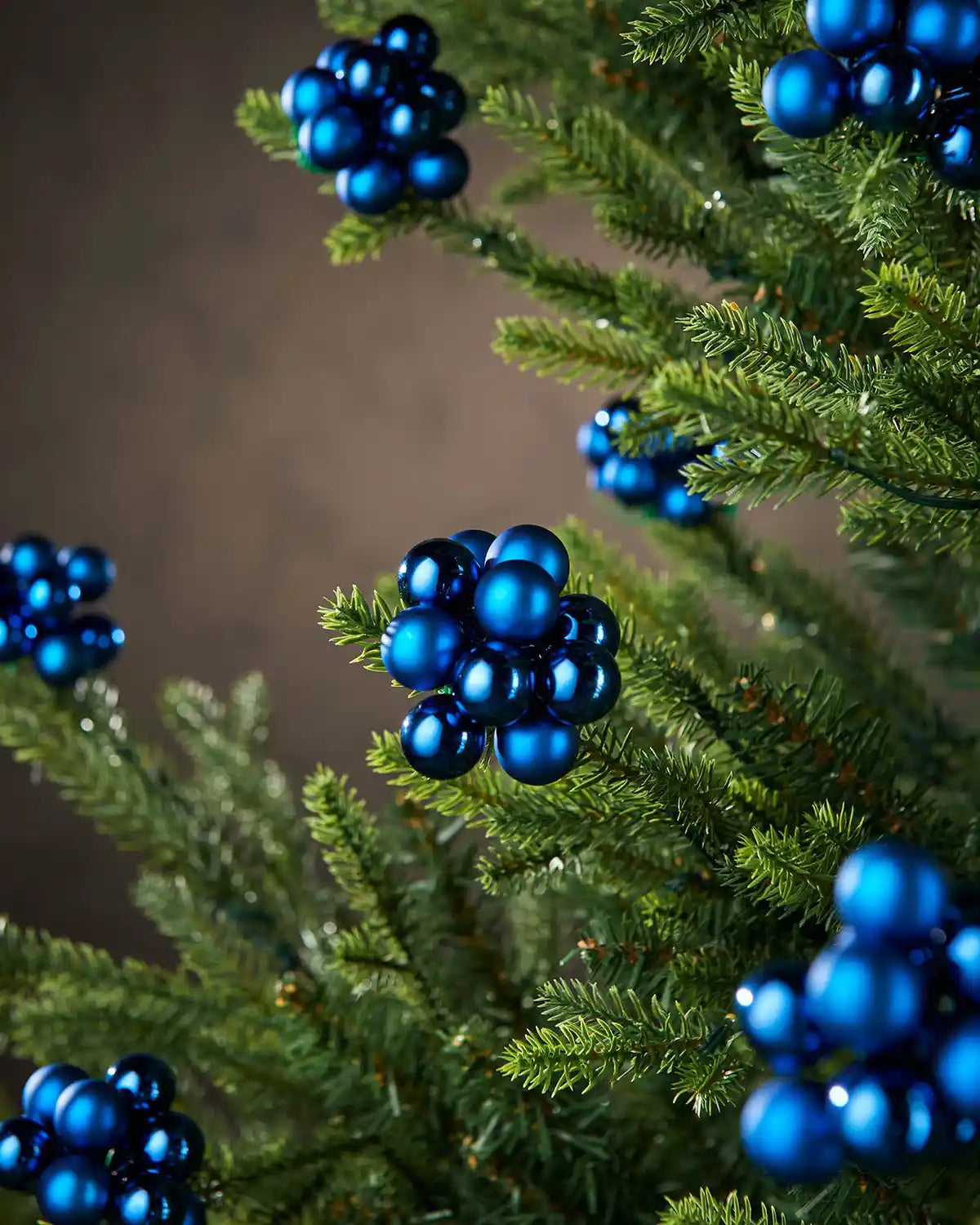 Blue berry ornaments on a Christmas tree against a neutral background