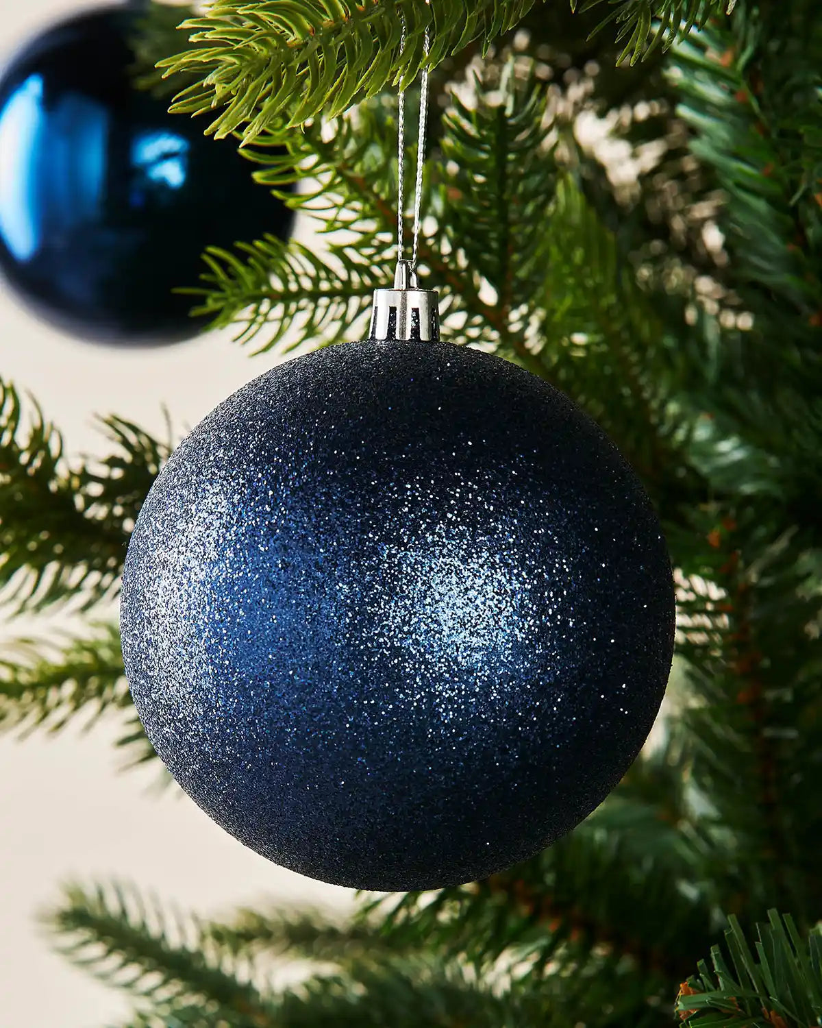 Blue glittery Christmas ornament hanging on a tree branch