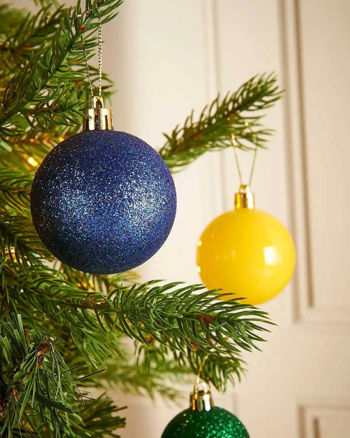 Blue, yellow, and green glittery Christmas baubles on a tree branch.