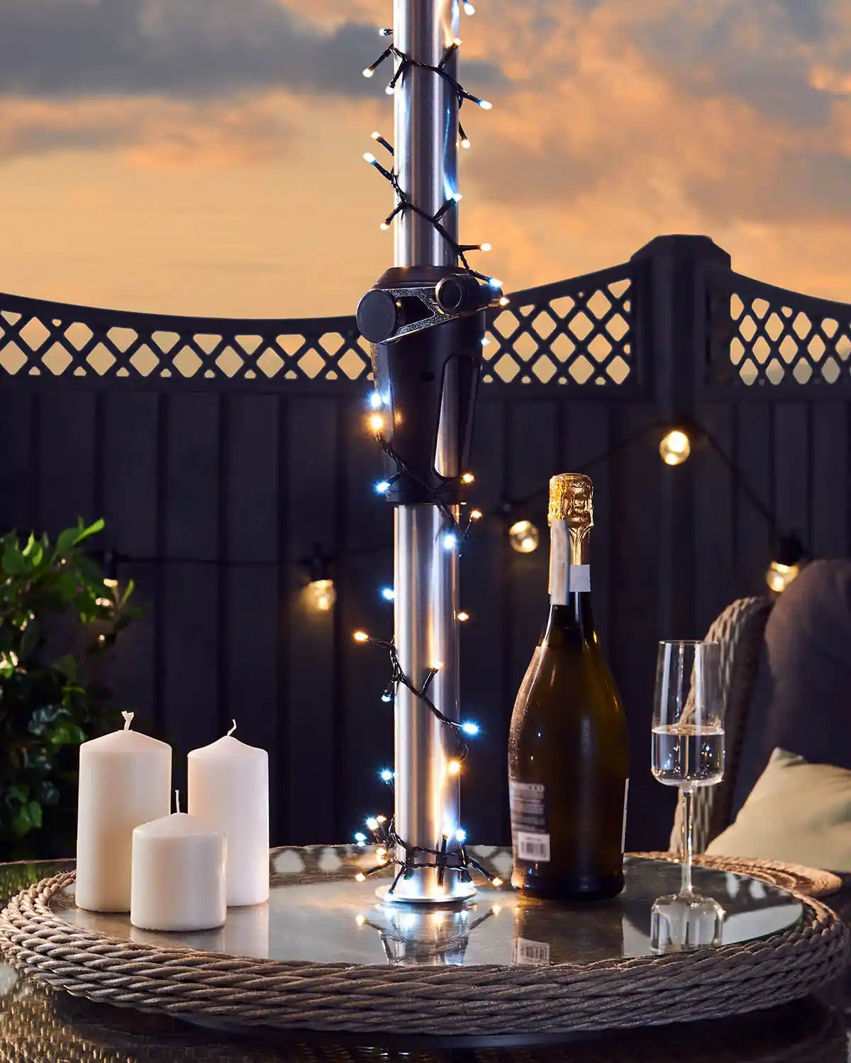 Bottle of champagne with a glass on a table decorated with  warm white and ice white fairy lights outdoors at sunset