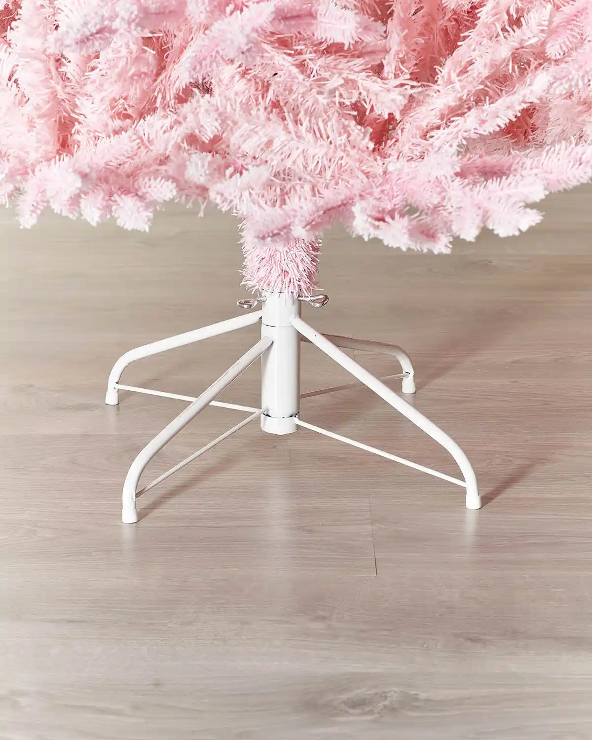 Bottom of a Pink artificial Christmas tree with white stand on a wooden floor