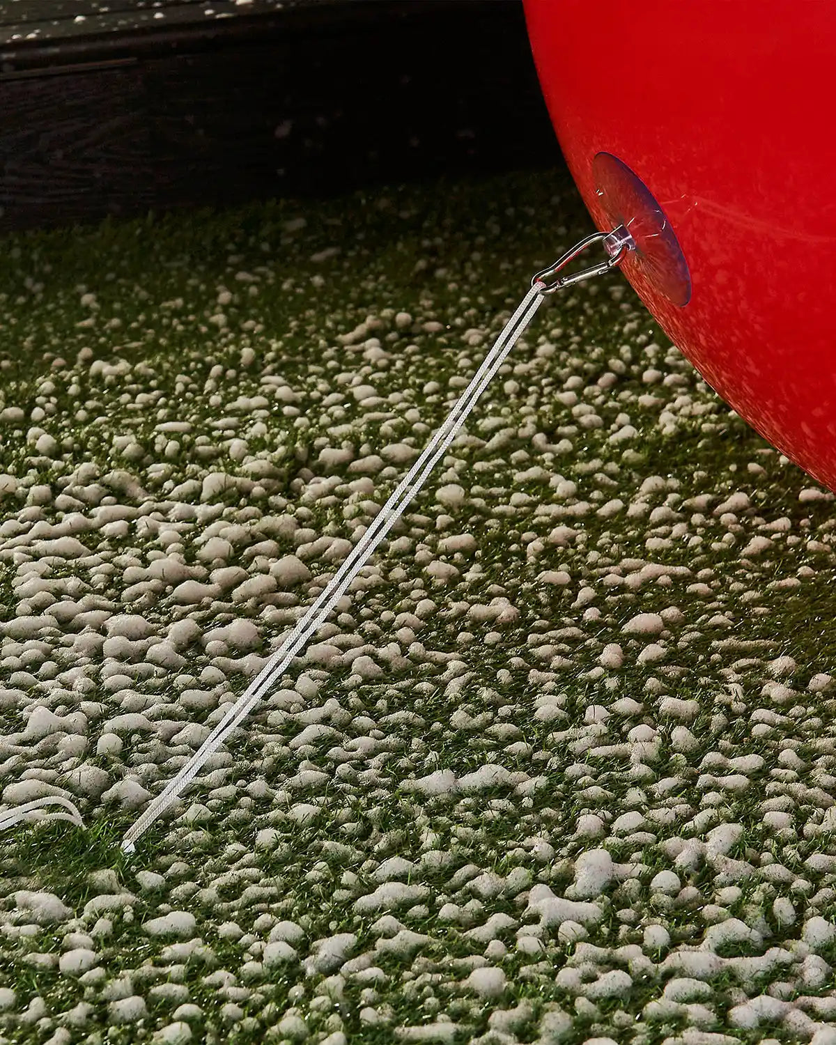 Bottom of extra large red inflatable bauble attached to an anchor into the ground with a garden stake against a snowy garden.
