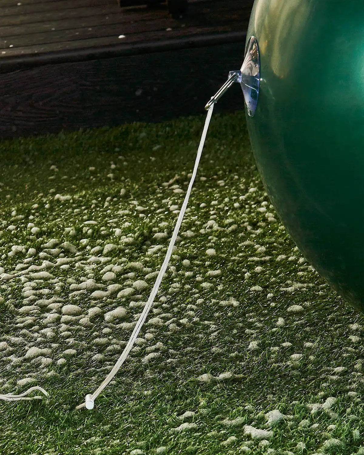 Bottom of large green inflatable bauble attached to an anchor into the ground with a garden stake against a snowy garden.
