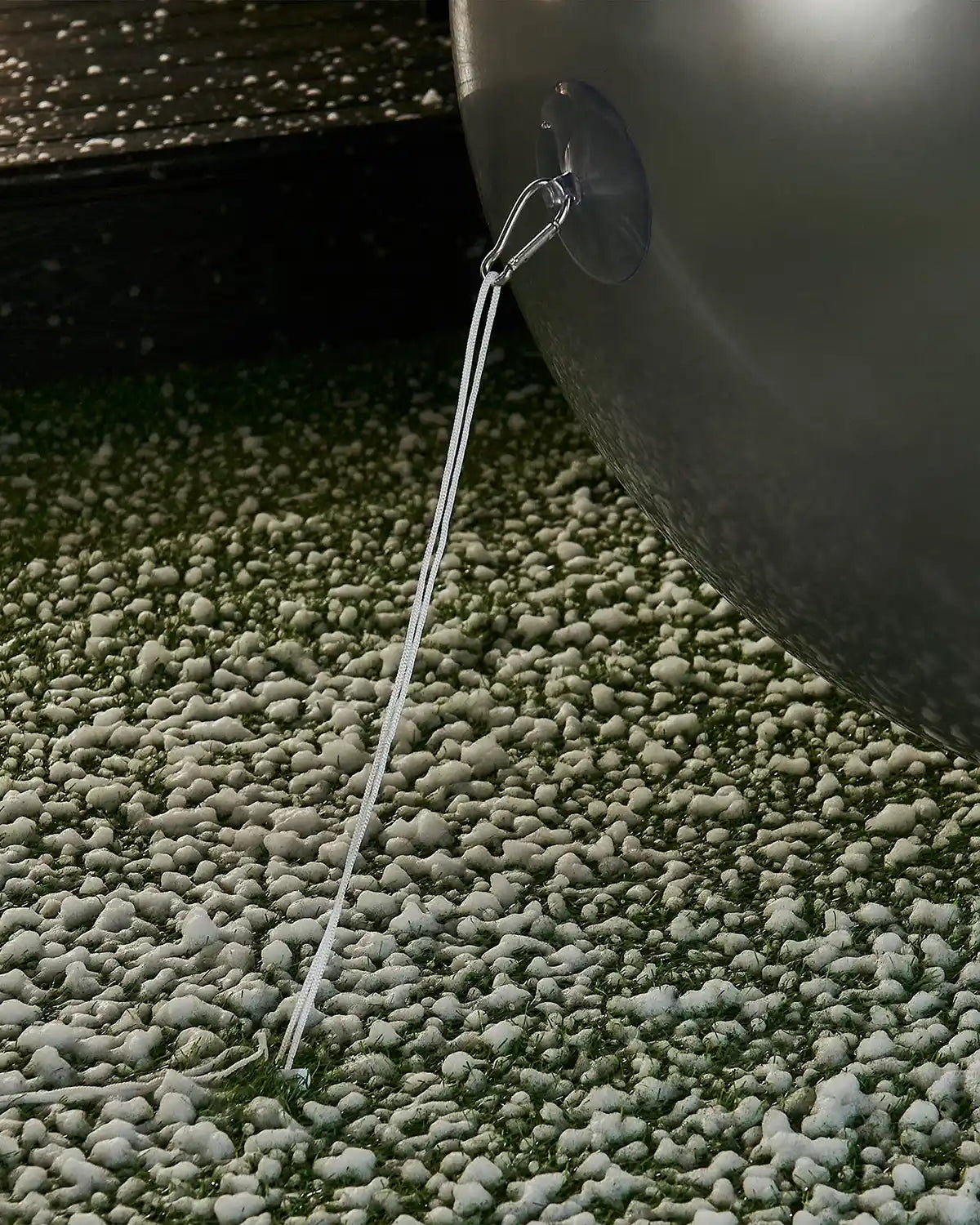 Bottom of large silver inflatable bauble attached to an anchor into the ground with a garden stake against a snowy garden.
