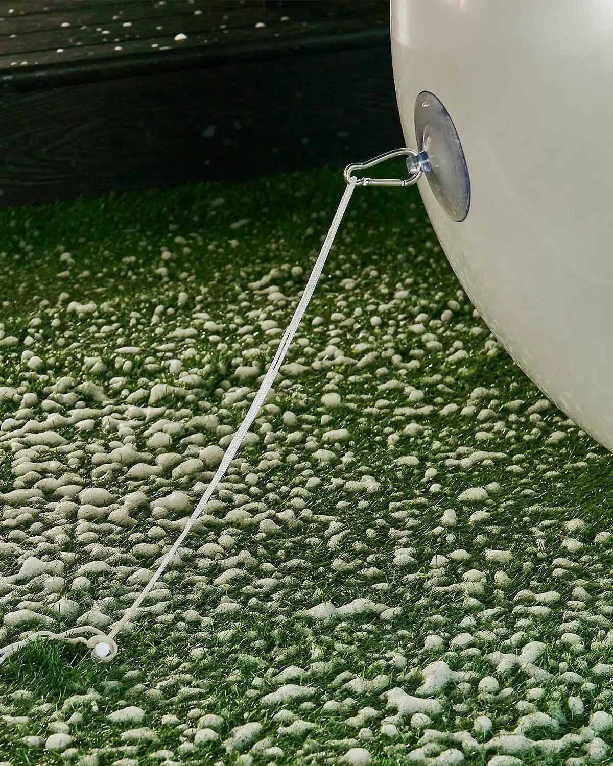 Bottom of large white inflatable bauble attached to an anchor into the ground with a garden stake against a snowy garden.
