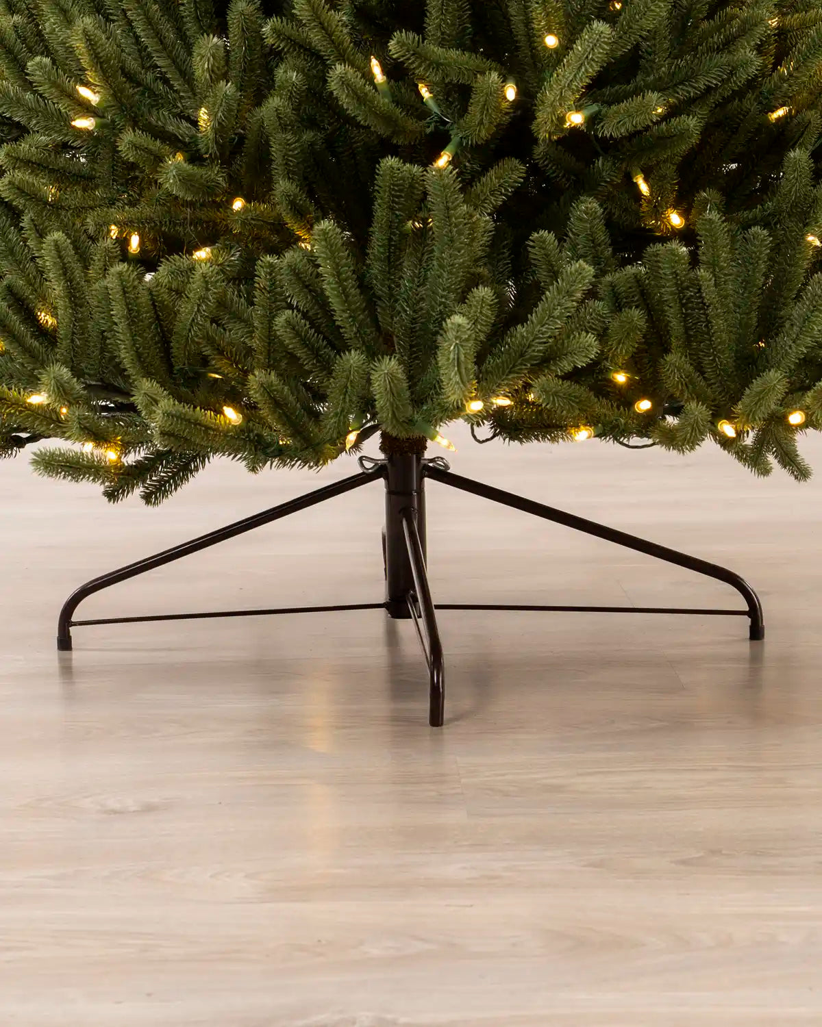 Bottom section of the Pre-Lit Empress Fir Christmas Tree, showing the black metal tree stand on a wooden floor
