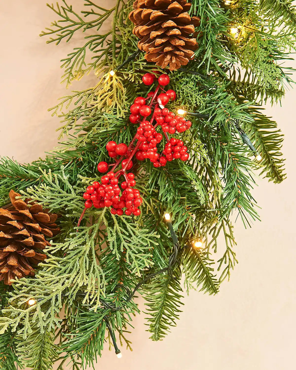 Bottom view Christmas wreath with greenery, red berries, and pinecones on a light background