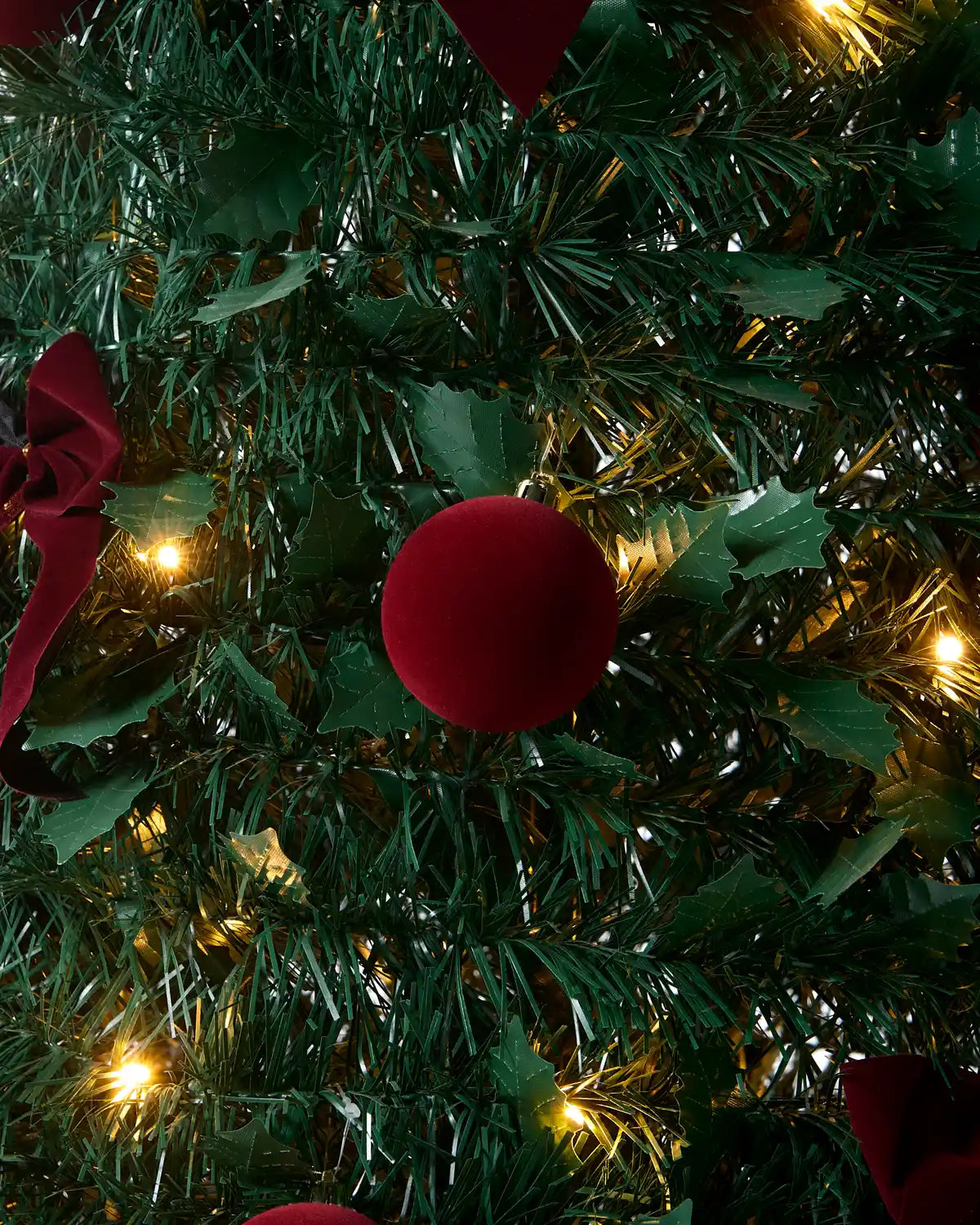 A large burgundy Christmas tree topper bow with gold trim, displayed on a green artificial Christmas tree.
