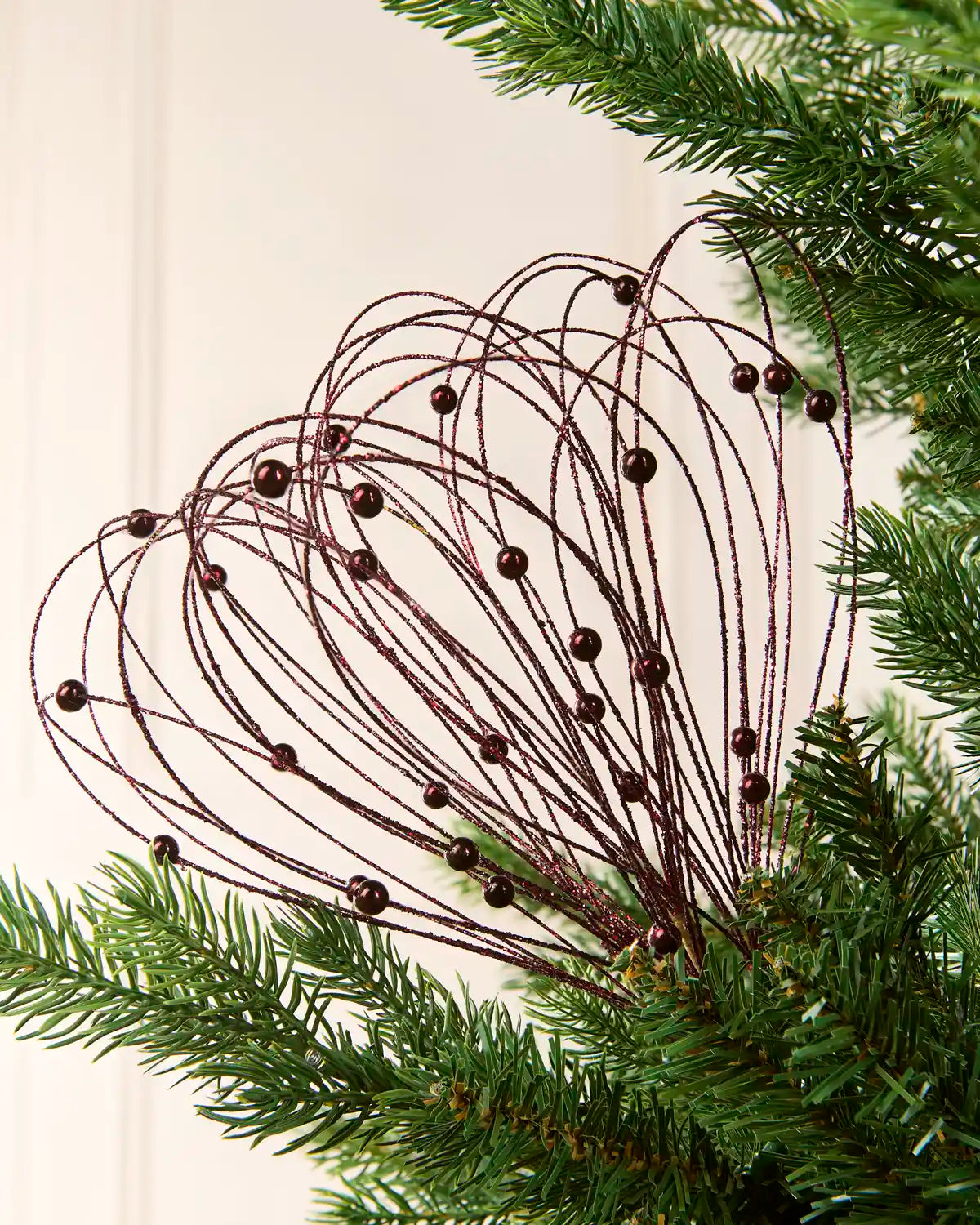 Burgundy Glitter Nest Christmas Tree Pick placed in green Christmas tree branches with a cream background
