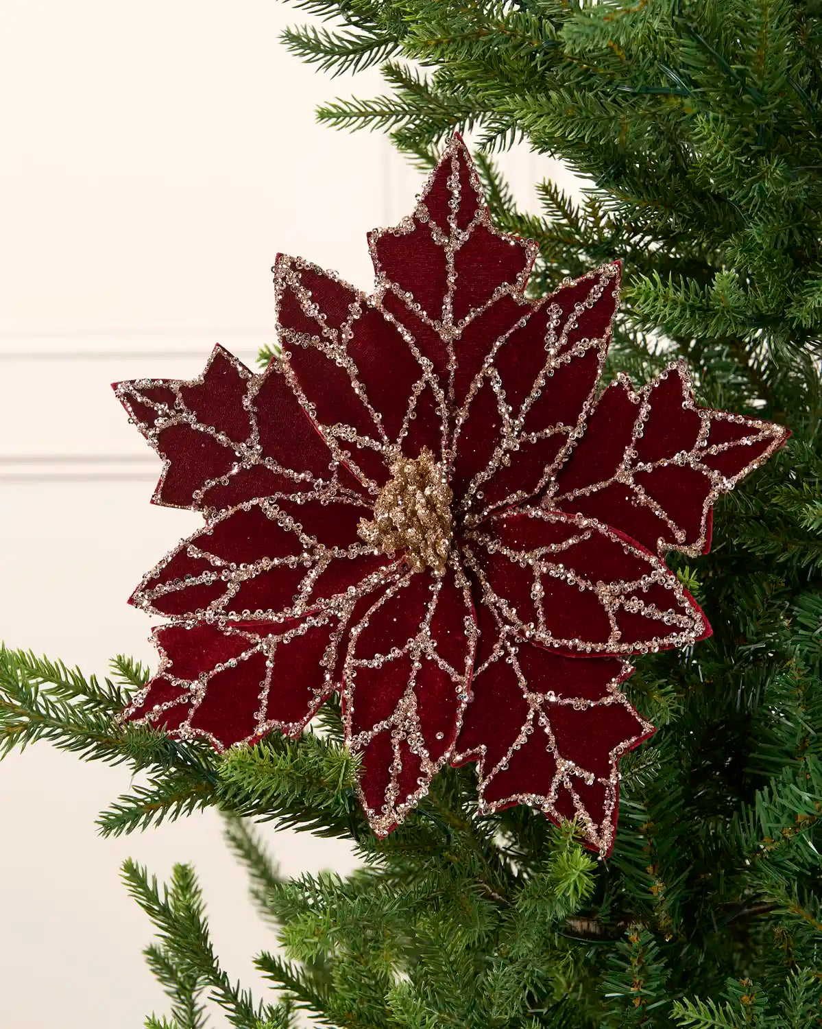 Burgundy and gold poinsettia flower on a Christmas tree against a cream background